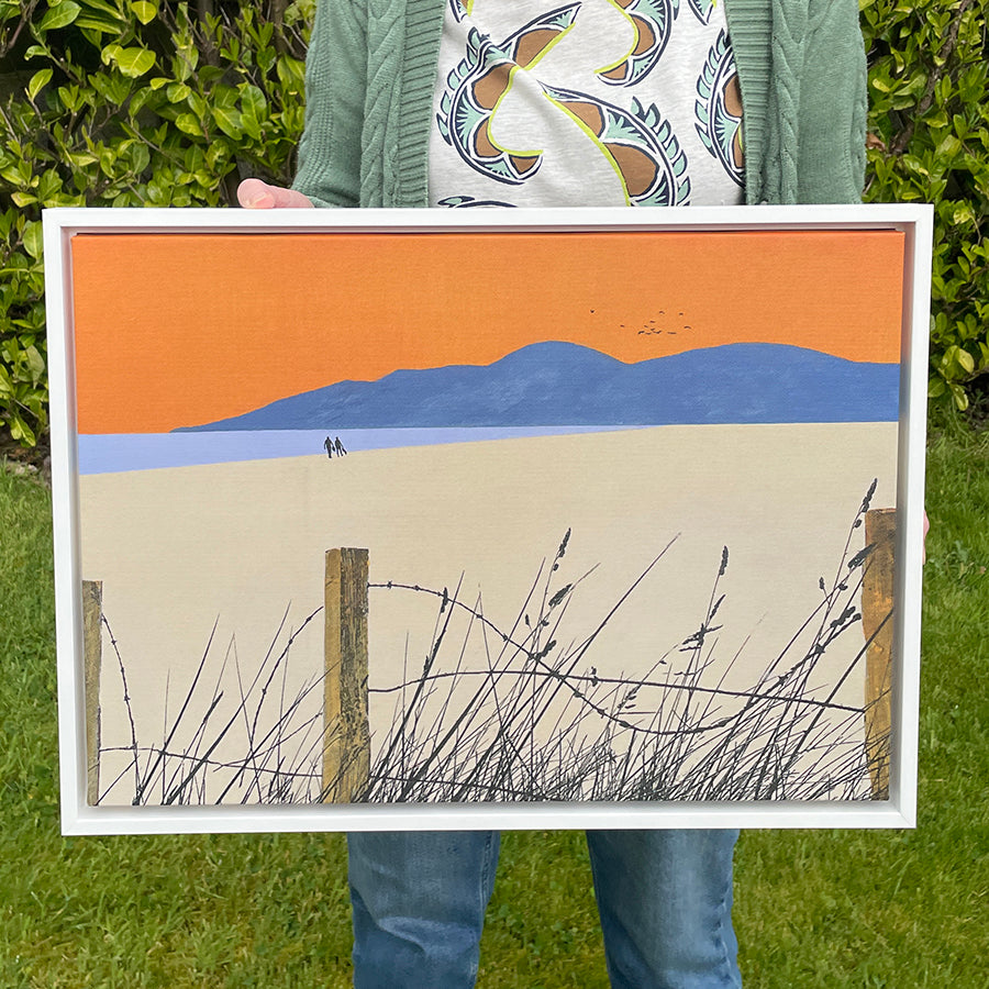 Landscape-oriented fine art canvas print titled A Shared Horizon by Norma Slack, showing a couple walking toward blue mountains under an orange sky with a lilac sea.