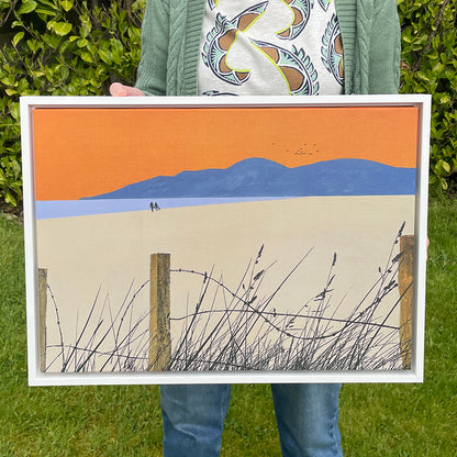 Landscape-oriented fine art canvas print titled A Shared Horizon by Norma Slack, showing a couple walking toward blue mountains under an orange sky with a lilac sea.